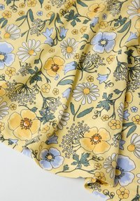 Blumenstoff mit gelben, blauen und weißen Blumen auf einem sanften gelben Hintergrund; leichtes, strukturiertes Material mit kunstvollen Details.