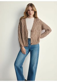 Sweter kardigan w jasnobrązowym kolorze z teksturowanym wzorem, z przodu zapinany na guziki, z długimi rękawami i lekko krótkim krojem. W zestawie z niebieskimi dżinsami o wysokim stanie.