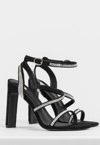 Sandali con tacco alto in suede nero, dotati di cinturini incrociati e accentuati da strass argentati, con un robusto tacco a blocco.