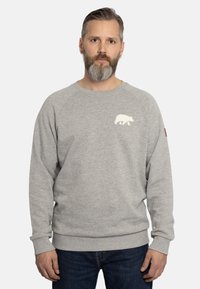 Felpa grigia realizzata in morbido tessuto, con una grafica di un orso bianco sul petto e polsini e orlo a coste. Abbinata a jeans in denim scuro.