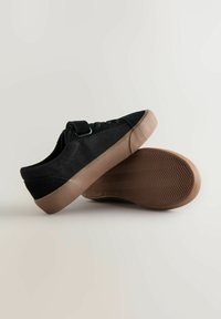 Scarpe nere in tela con un esterno testurizzato, dotate di una fascia in velcro e una suola in gomma marrone chiaro con un motivo a spina di pesce.