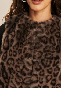 Bruin en zwart luipaardprint nepbont sjaal gedragen door een vrouw met golvend haar en gouden hoop oorbellen.