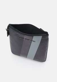 Crni zippered neseser sivi naglasci. Sadrži ugravirani logo i teksturiranu površinu. Unutrašnjost obložena crnom tkaninom.
