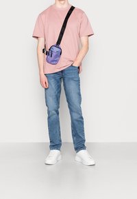 T-shirt rosa a maniche corte, jeans blu, sneaker bianche e una borsa a spalla viola con tracolla nera e tasche con zip. Design semplice.