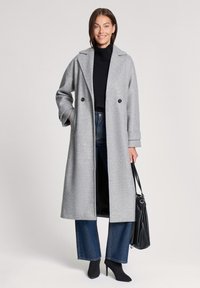 Szary wełniany płaszcz z klapowym kołnierzem, podwójnymi guzikami i bocznymi kieszeniami, w połączeniu z czarnym golfem i dżinsami o szerokich nogawkach.
