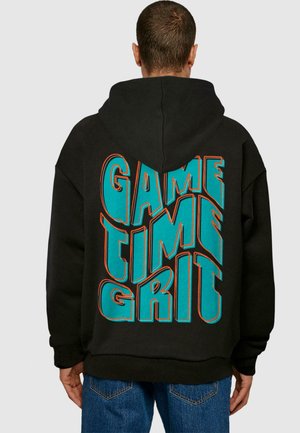 Schwarze Kapuzenjacke mit großem türkis- und orangefarbenem Text auf dem Rücken, der "GAME TIME GRIT" liest. Warmes Material, lockere Passform und angenähte Kapuze.