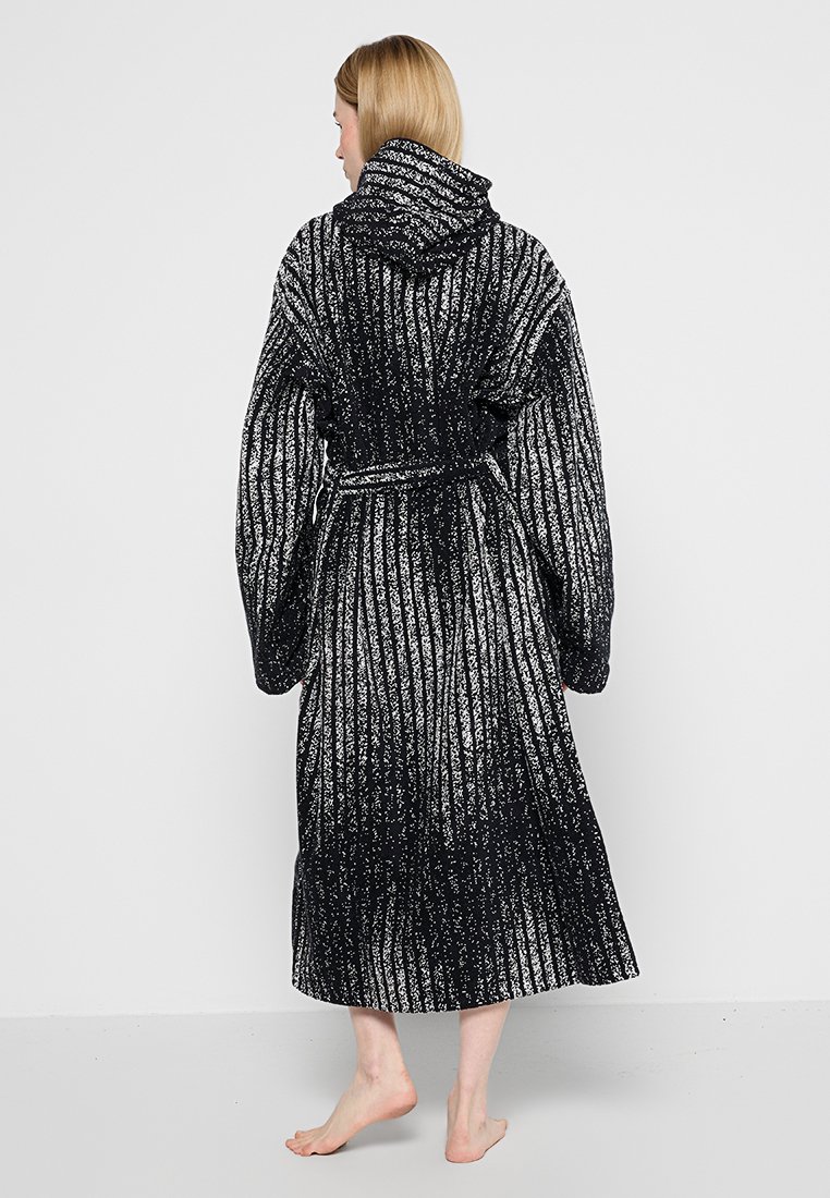 Lunga veste nera e bianca con cappuccio, caratterizzata da un design a coste testurizzate, con cintura annodata in vita e maniche aperte. Tessuto comodo e caldo.