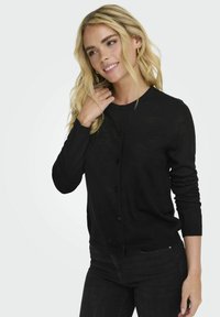 Melnā kardigāna izgatavots no viegla adījuma. Iespējas: apaļa kakla izgriezums, garas piedurknes un priekšējā pogu aizdare ar slaidu piegriezumu.