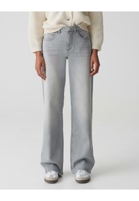 Lichtgrijze wijde jeans met een hoge taille, voorzien van een knoopsluiting, voormokken en een faded wassing, gecombineerd met witte sneakers.