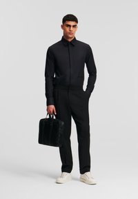 Schwarzes Langarmshirt, kombiniert mit schwarzen Hosen, hält eine strukturierte schwarze Tasche. Die Schuhe sind off-white mit einer glatten Oberfläche. Einfaches Design.