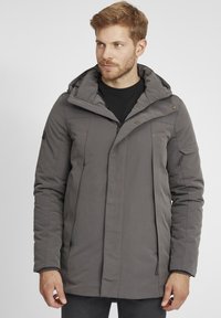 Chaqueta de abrigo gris con capucha, con cierres de cremallera y botón, bolsillos laterales y una textura suave. Diseño sencillo con acentos mínimos.