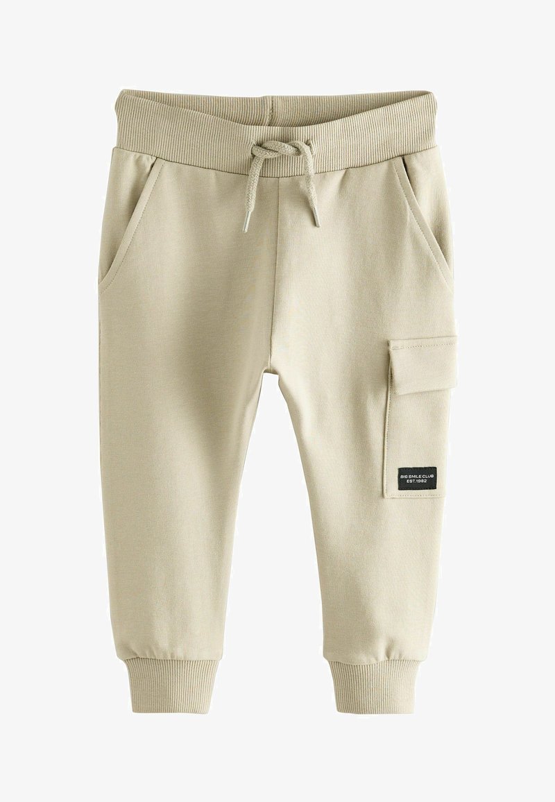 Pantaloni della tuta beige per bambini con cintura a costine, coulisse, tasche frontali, polsini alle caviglie e tasca laterale con etichetta nera.
