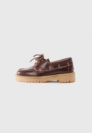 Chaussure bateau en cuir marron avec un bout arrondi, un laçage à l'avant et des œillets en métal, dotée d'une semelle épaisse de couleur marron clair et de coutures contrastées.