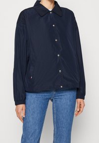 Tmavě modrá bunda vyrobená z lehkého materiálu, s límcem, patentkami a elastickými manžetami. Obsahuje postranní kapsy.