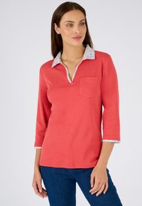 Top de manga larga color coral con un cuello y puños de estampado floral, con escote en V y un bolsillo delantero. Material de algodón suave.