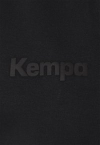Tessuto nero con una superficie a maglia testurizzata presenta un prominente logo in gomma nera "Kempa" centrato sul capo.