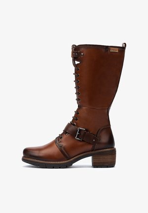 Botte en cuir marron haute avec des lacets, une sangle au niveau de la cheville avec une boucle en métal, un petit talon empilé et une semelle en caoutchouc, marquée "Pikolinos" près du bord supérieur.