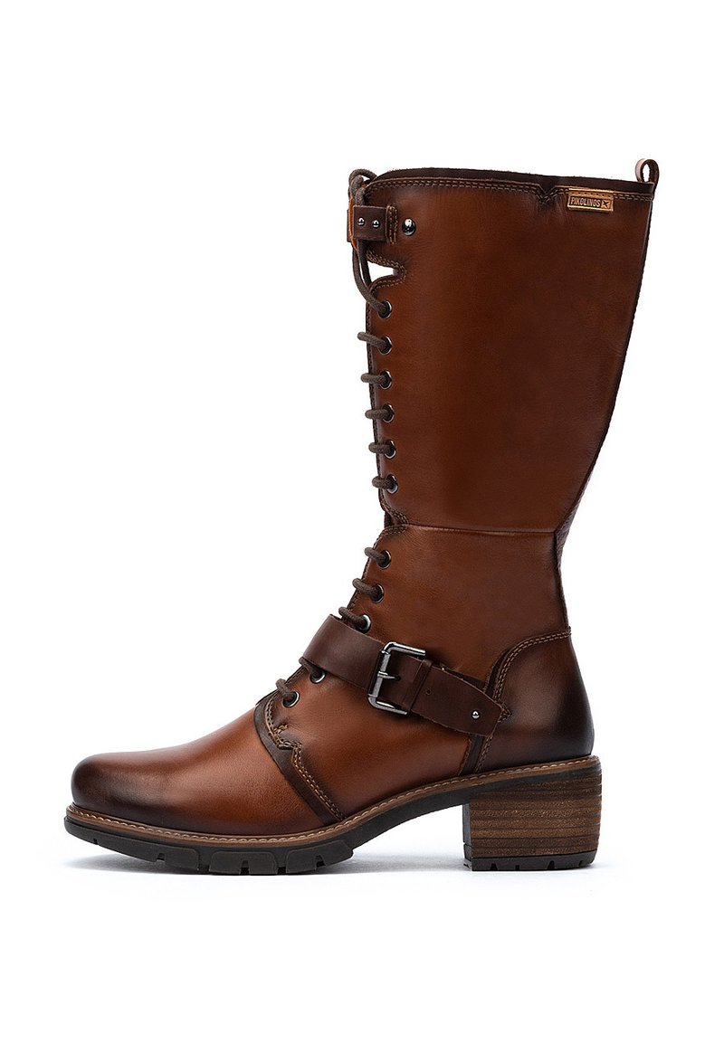 Botte en cuir marron haute avec des lacets, une sangle au niveau de la cheville avec une boucle en métal, un petit talon empilé et une semelle en caoutchouc, marquée "Pikolinos" près du bord supérieur.
