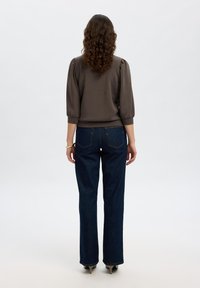 Top marrone con maniche a sbuffo abbinato a jeans a campana blu scuro. Tessuto liscio, dettagli minimi e hardware denim classico.
