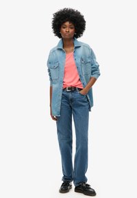 Chaqueta de mezclilla de color azul claro sobre una camiseta coral, jeans azul de talle alto, zapatos negros y un peinado afro. Un outfit sencillo y casual.