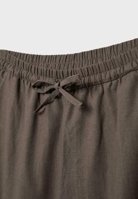 Taille élastique avec cordon en tissu noué sur un pantalon léger brun foncé.