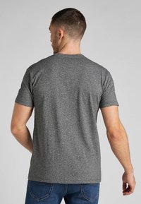 Grå kortærmet t-shirt med rund halsudskæring, der har et tekstureret stof og en lige kant, båret med blå jeans.