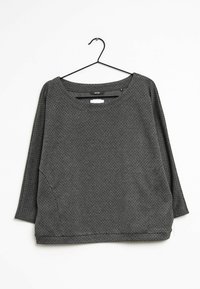 Camisa de manga larga de patrones en negro y gris con un escote amplio y un corte holgado, colgando de una percha de metal negro sobre un fondo blanco.