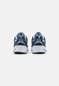 Mörkblå träningsskor med meshovandel, vita detaljer och vadderad vit sula. Har en vadderad krage och hälflik för lätt påtagning.