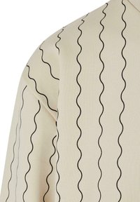 Suéter beige con líneas negras en forma de onda. Textura suave y cuello acanalado. La vista de cerca se centra en el patrón y la forma de la manga.