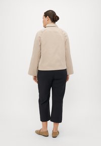 Beige lett jakke med spiss krage, lange ermer og strukturert passform, kombinert med svarte cropped bukser og brune leiligheter.