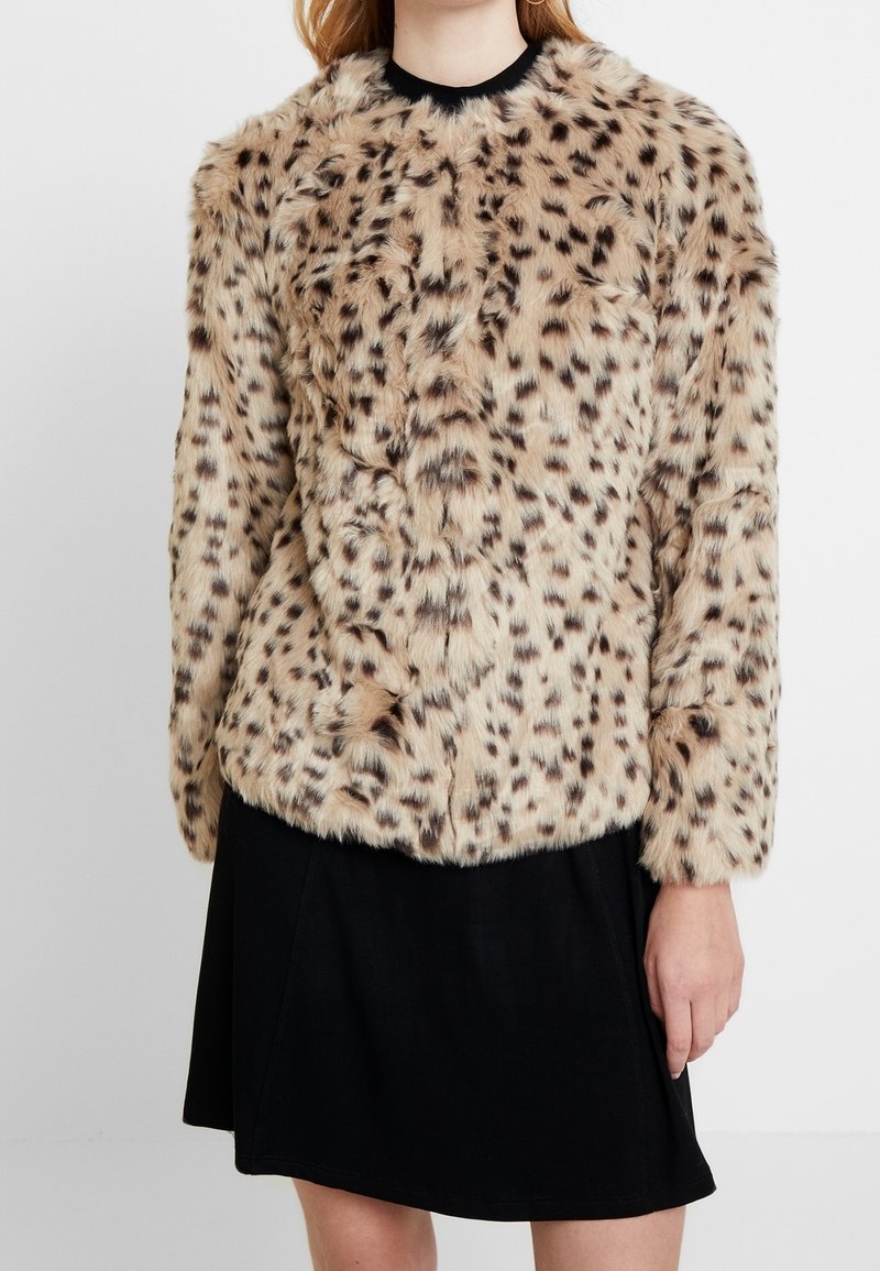 Tekoturkista valmistettu takki vaaleanruskeana, jossa on leopardikuosiset yksityiskohdat. Takissa on pitkät hihat ja pyöreä kaula-aukko. Pehmeä rakenne ja rento istuvuus.