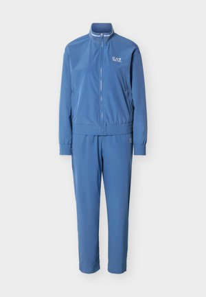 Kék cipzáras melegítő felső rugalmas mandzsettákkal és derékpánttal, amelyen EA7 Emporio Armani logó található a mellkason és a combon.