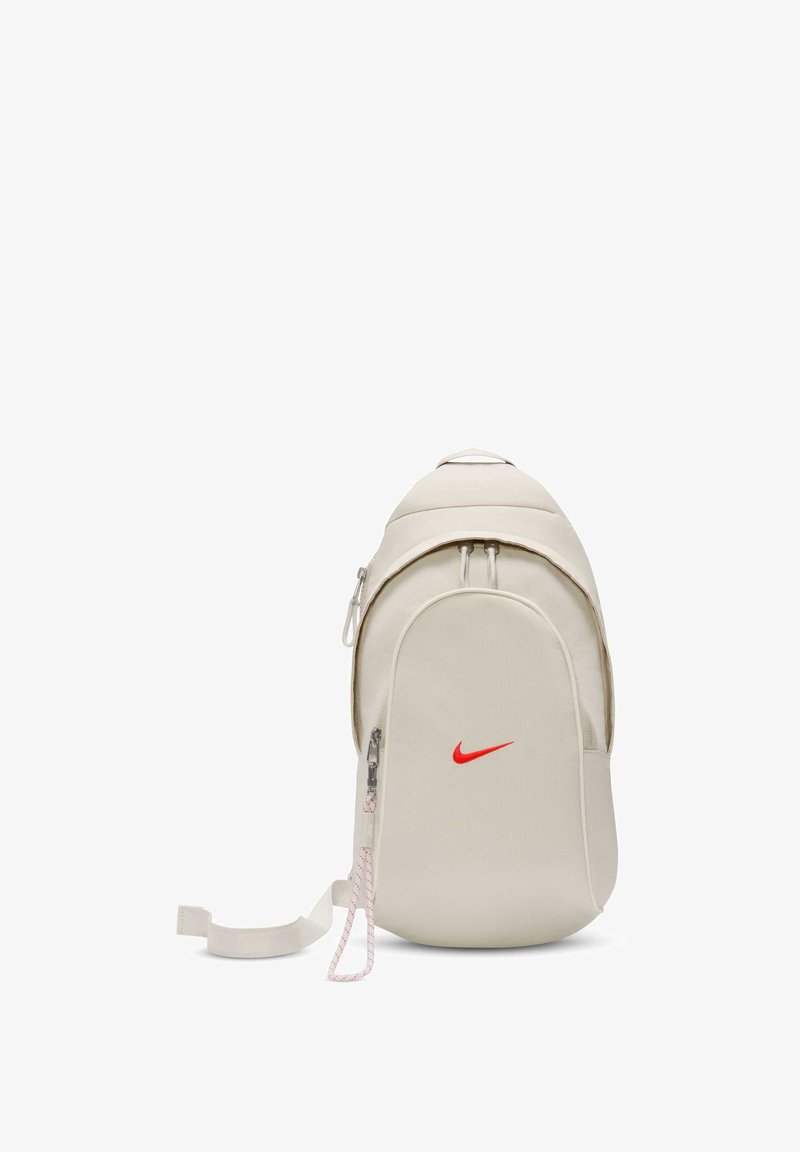 Nike-ryggsäck i off-white tyg med en framträdande röd logotyp, slät rundad form, dragkedjeavdelningar och strukturerade band.