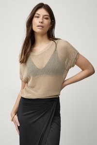 Beige gaasgebreide top met korte mouwen en een ronde halslijn, gelaagd over een zwarte cami, gecombineerd met een zwarte wikkelrok.
