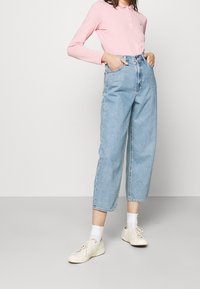 Ljusrosa långärmad polo med krage, i kombination med högmidjade blå jeans och vita sneakers med vita strumpor.