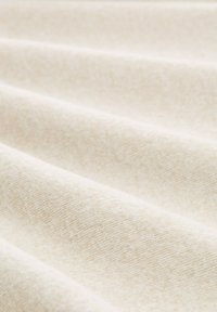Tissu beige avec une texture douce, présentant des lignes diagonales subtiles et une surface lisse. Le matériau semble léger et malléable.