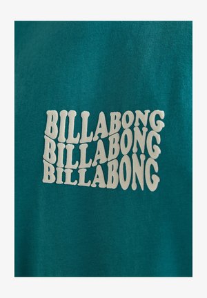 Türkise Baumwoll-T-Shirt mit wiederholtem weißen "BILLABONG"-Textdesign in einer geschwungenen Schriftart. Der Stoff hat eine weiche Textur.