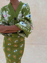 Cardigan vert à motifs avec des motifs d'yeux et une fermeture à boutons, associé à une jupe assortie ornée de fleurs et d'yeux dans des teintes similaires.
