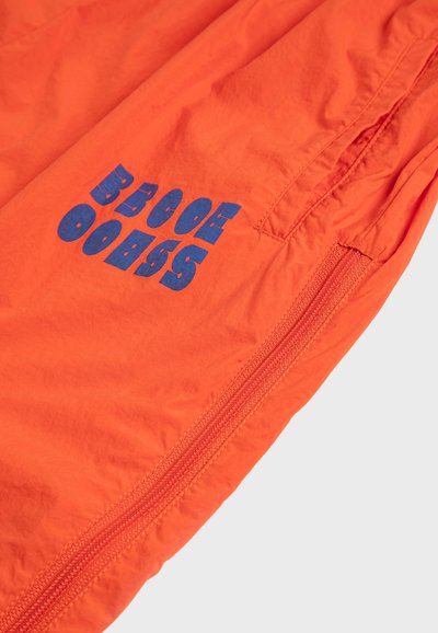 Tissu orange vif avec un détail de fermeture éclair et un texte bleu audacieux disant "DEVENEZ PATRON" dans une police stylisée.