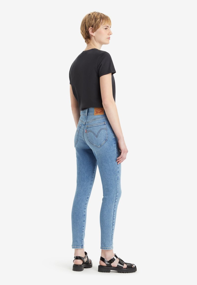 T-shirt noir à manches courtes associé à un jean skinny taille haute bleu clair. Des sandales noires à semelle épaisse complètent la tenue.