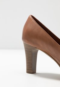 Scarpa con tacco alto in pelle marrone, punta affusolata, finitura testurizzata, tacco a blocco in stile legno e cuciture pulite lungo i bordi.