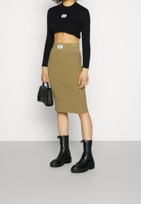 Svart ribbad crop top med rund halsringning, tillsammans med en khaki ribbad BÅLkjol och svarta ankelstövlar. Bär en liten svart handväska.