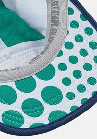 Green and white patterned cap with large circular designs, grey inner lining, and a blue rim. Made of textured fabric.