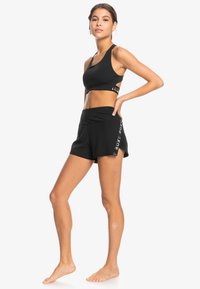 Zwart sportief crop top met een racerback ontwerp en hoge zwarte shorts met zijzakken en witte logo-accenten aan de zoom.