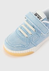 Baskets en denim bleu clair avec lacets blancs, bande Velcro et semelle en caoutchouc. Présente des accents cousus et une surface texturée.