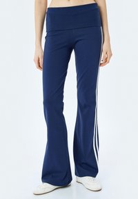 Marineblauwe flared broek met een brede tailleband, voorzien van witte zijstrepen. Gemaakt van rekbare stof voor comfort en bewegingsvrijheid.