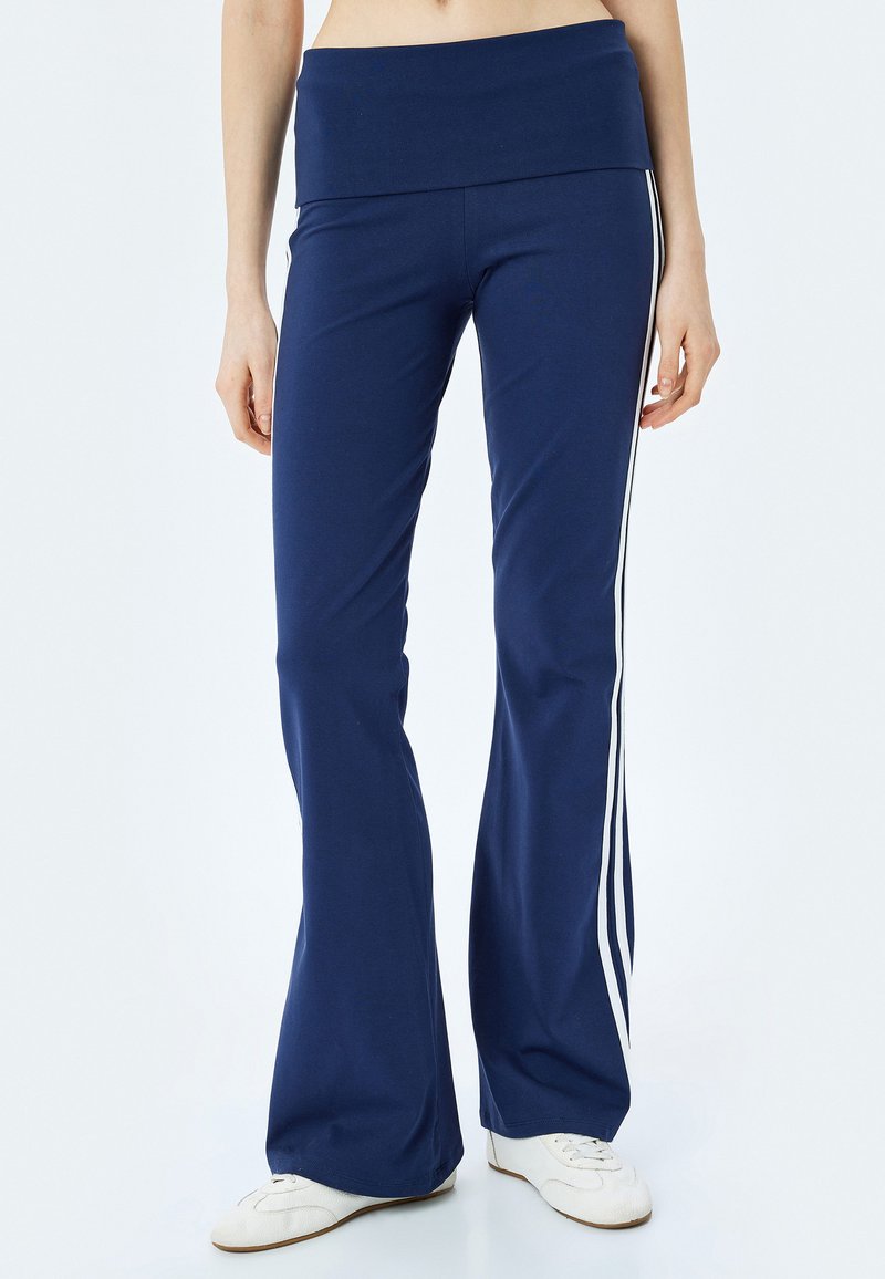 Marineblauwe flared broek met een brede tailleband, voorzien van witte zijstrepen. Gemaakt van rekbare stof voor comfort en bewegingsvrijheid.
