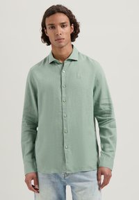 Camisa de manga larga verde claro con un ajuste relajado, botonadura frontal y un logo sutil en el pecho. Fabricada con una tela texturizada.