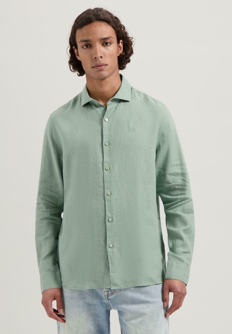 Camisa de manga larga verde claro con un ajuste relajado, botonadura frontal y un logo sutil en el pecho. Fabricada con una tela texturizada.