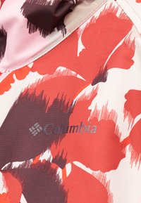 Λογότυπο Columbia σε ύφασμα με μεγάλο αφηρημένο κόκκινο, μαύρο και λευκό ανθικό σχέδιο, κοντινή λήψη που δείχνει λεπτομέρειες ραφής.